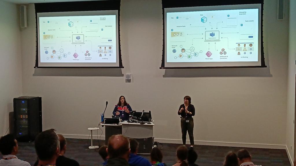 April Dunnam presenting at Scottish Summit 2022 with an interpreter. On the background are 2 large screens with her presentation