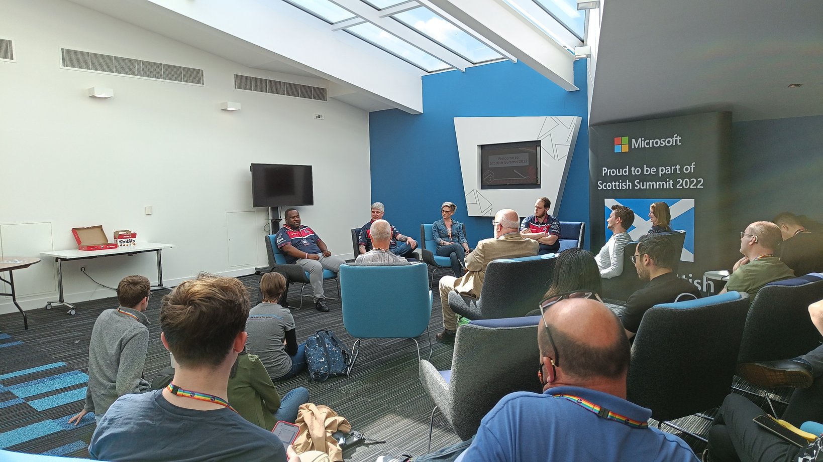 Community roundtable event at Scottish Summit. 4 people sitting in front of many spectators and a sign from Microsoft, saying that they are proud to be part of Scottish Summit 2022