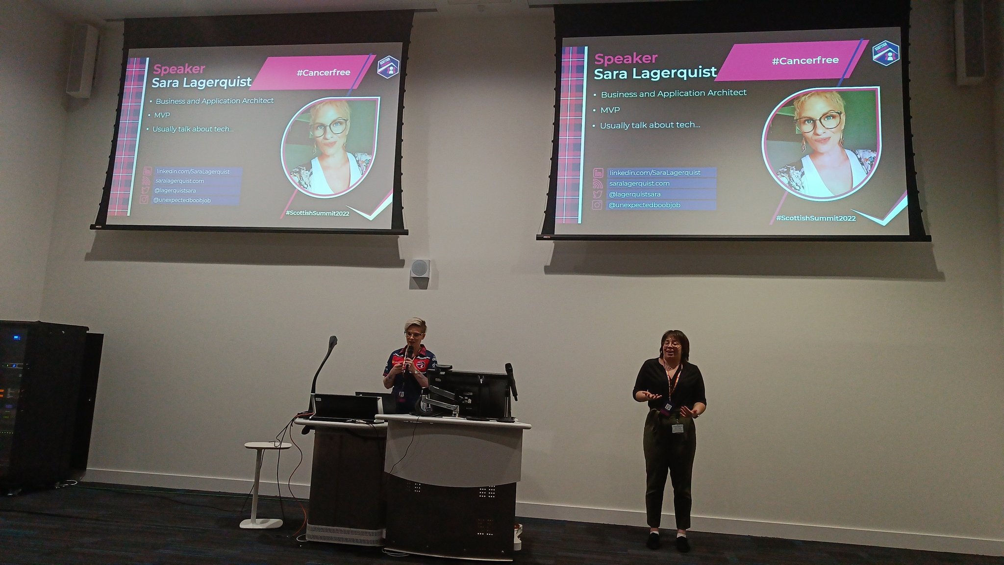 Sara Lagerquist presenting at Scottish Summit 2022 with an interpreter. On the background are 2 large screens with her presentation