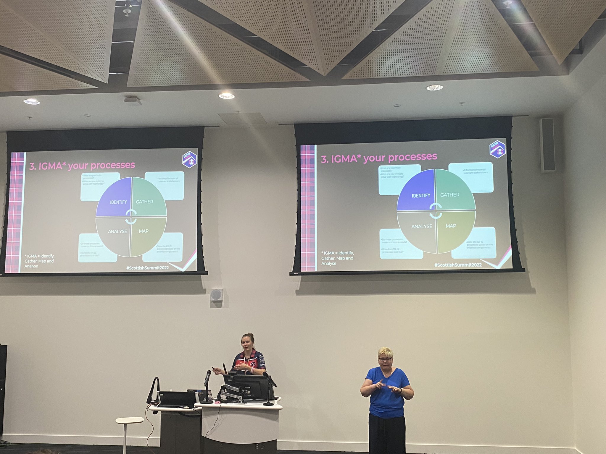 Vivian Voss presenting with an interpreter with 2 large screens on the background with her presentation